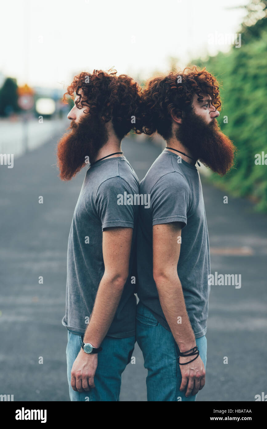 Portrait de jumeaux mâles adultes identiques aux cheveux rouges et barbes dos à dos sur le trottoir Banque D'Images