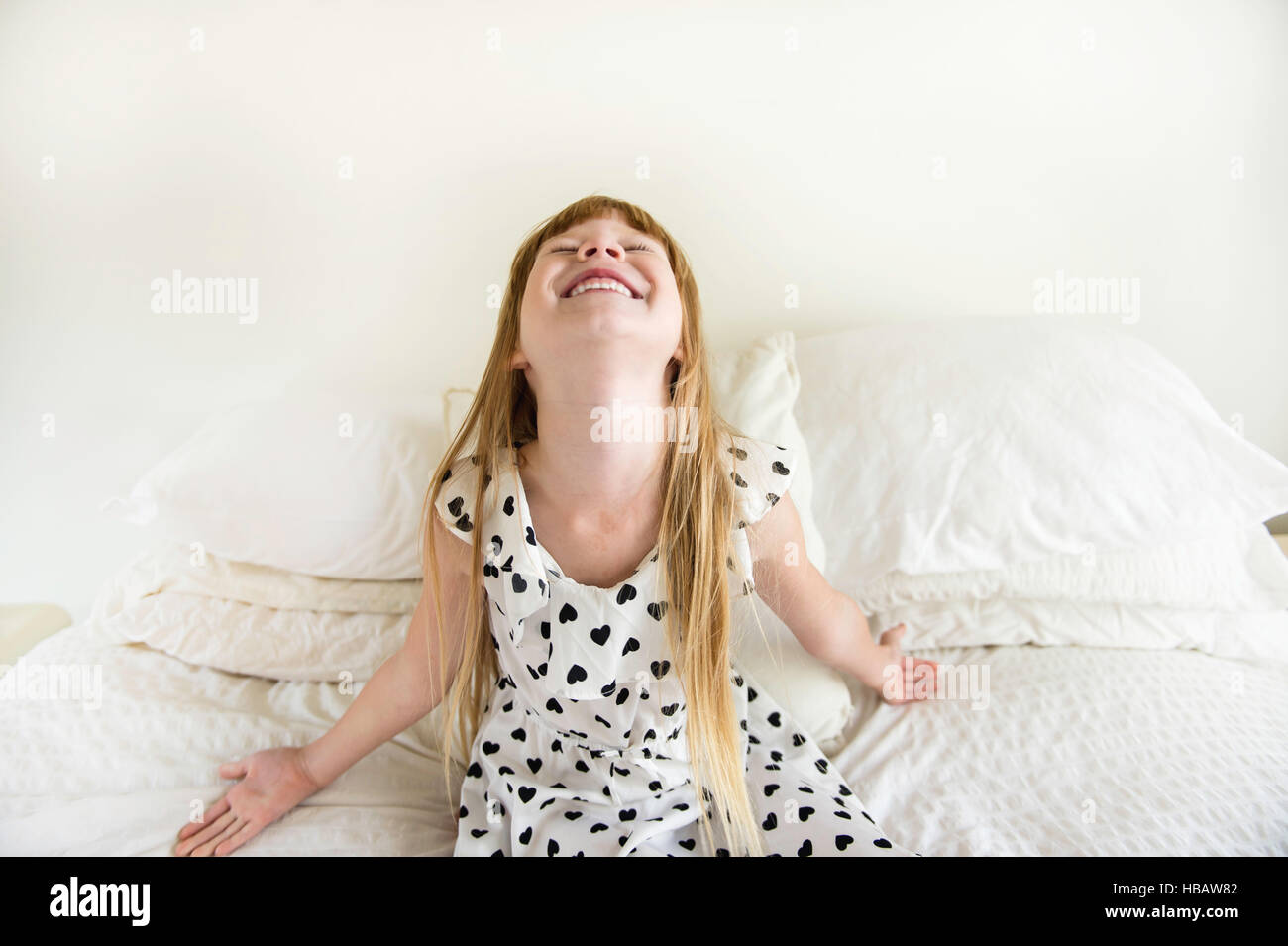 Jeune fille assise sur le lit de jeter tête en arrière Banque D'Images