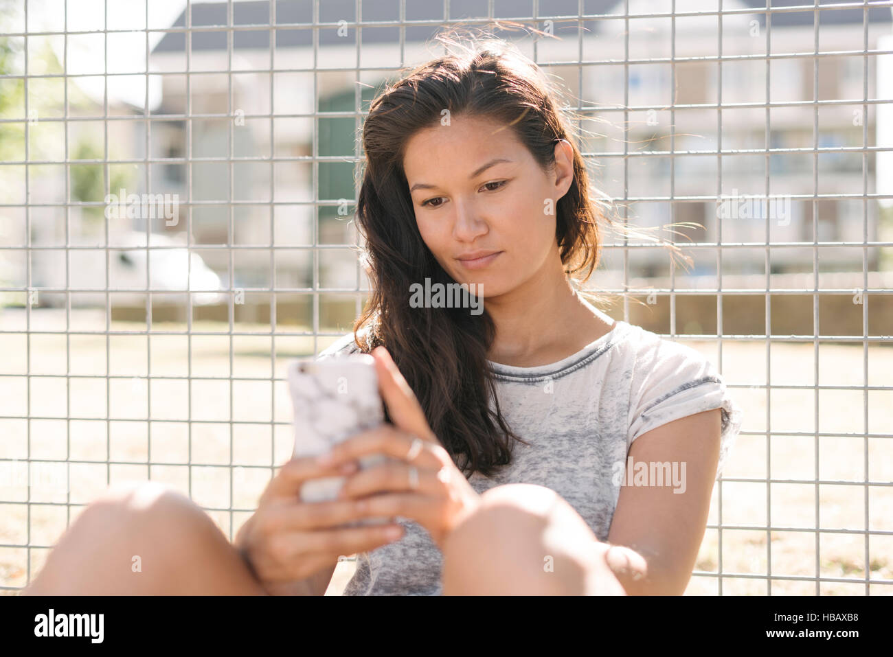 Femme lisant mises à jour smartphone par wire fence Banque D'Images