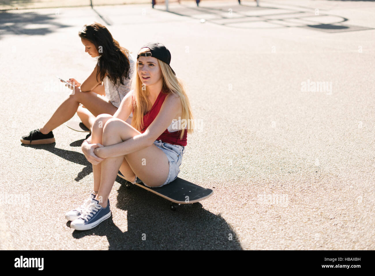 Deux amis femelles adultes assis sur une planche à roulettes sur un terrain de basket-ball Banque D'Images