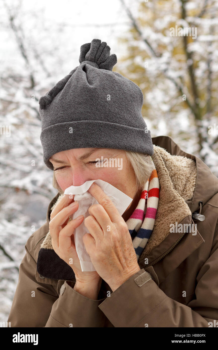 Hauts femme avec foulard et un chapeau dans une veste d'hiver s'être mouché le nez dans un mouchoir en papier en face d'un arbre avec de la neige Banque D'Images