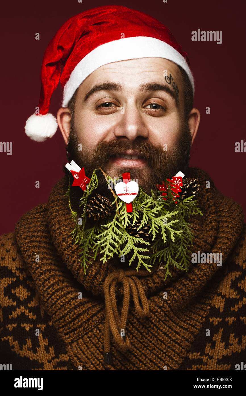 Homme barbu rigolo dans une nouvelle image de l'année en père Noël avec des décorations sur sa barbe. Fête de Noël. Banque D'Images