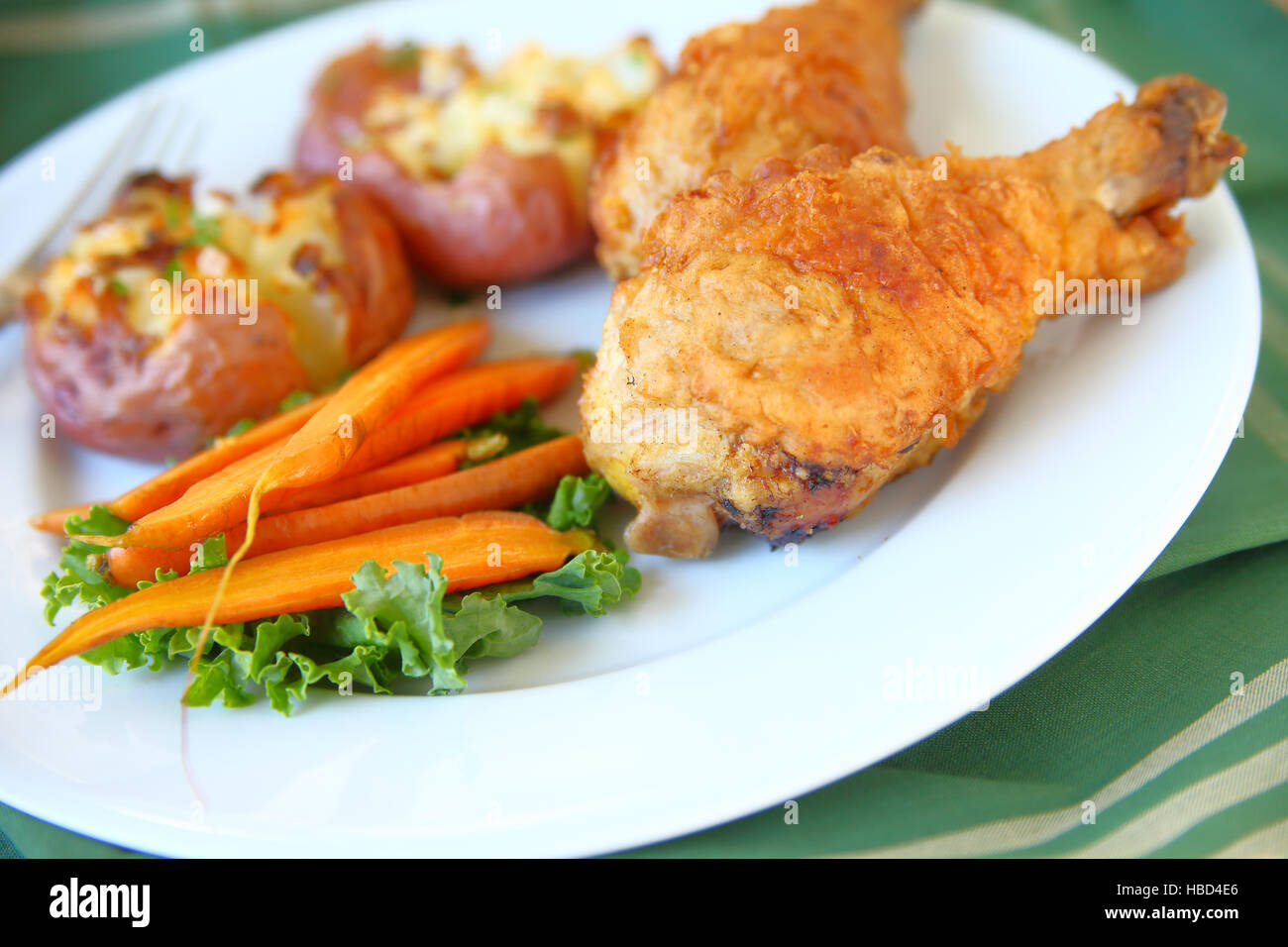 Le poulet frit, les carottes et les pommes de terre rôties concassées sur une plaque blanche avec serviette Banque D'Images