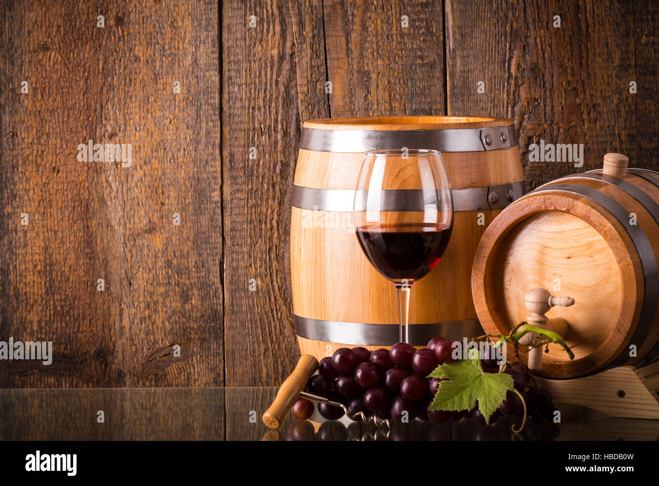 Verre de vin rouge avec des barils et des raisins sur verre avec fond de bois Banque D'Images