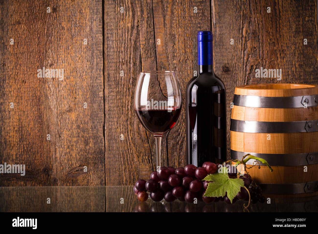 Verre de vin rouge avec une bouteille en verre avec fourreau raisins sur fond de bois Banque D'Images