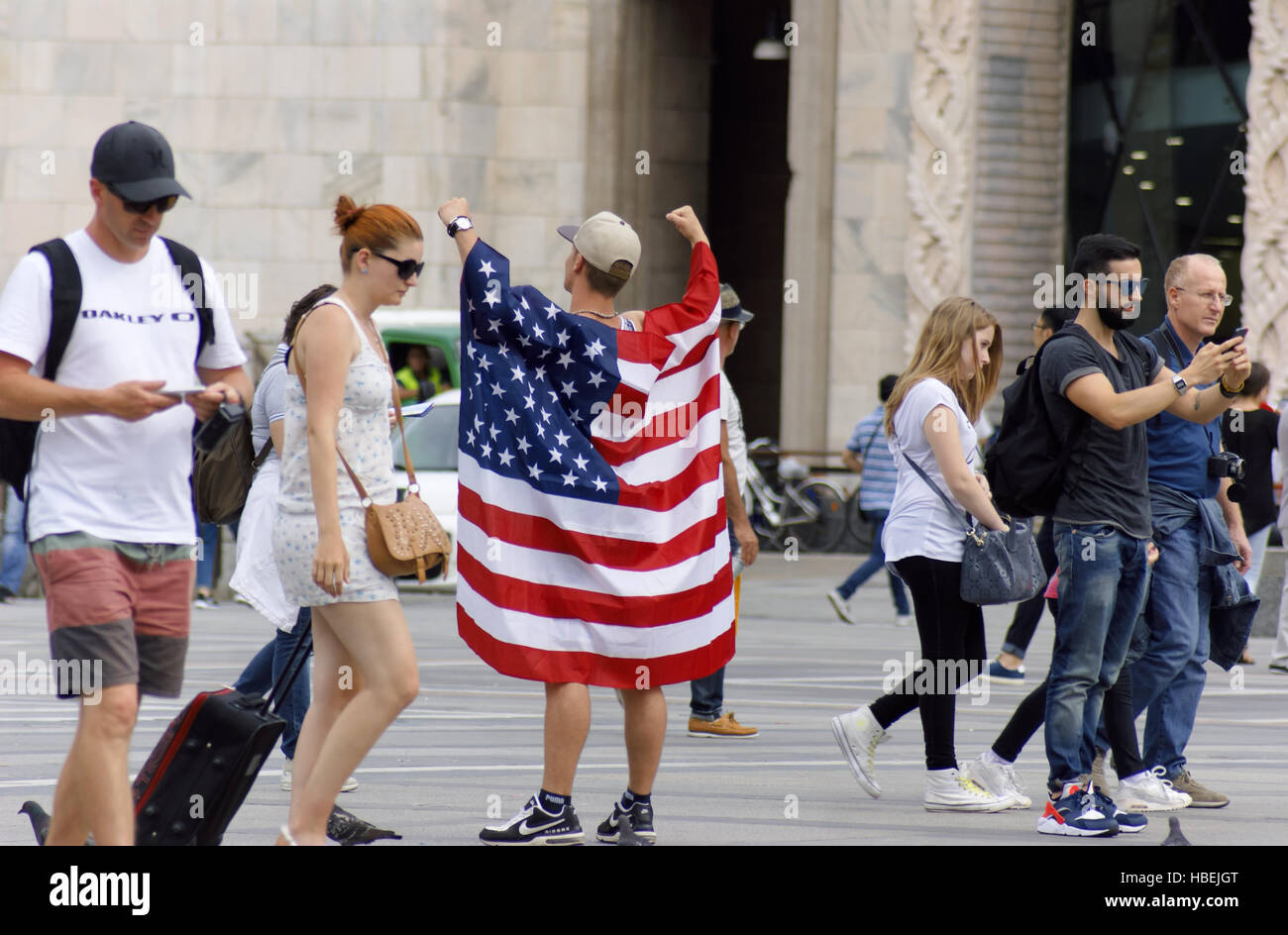 L'homme drapé dans le drapeau de l'United States avec bras levés au milieu de la Piazza del Duomo, Milan, Italie. Banque D'Images