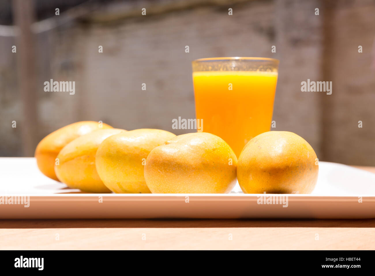 Jaune à maturité paraguayenne de mangues et de tasse de jus de mangue fraîche sur le plateau blanc, table en bois, sous la lumière du soleil lumineuse Banque D'Images