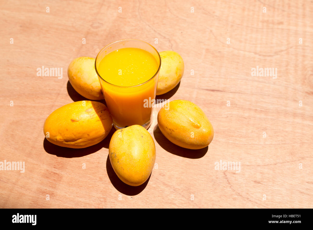 Jaune à maturité paraguayenne de mangues et de tasse de jus de mangue fraîche sur la table de bois, sous la lumière du soleil lumineuse Banque D'Images