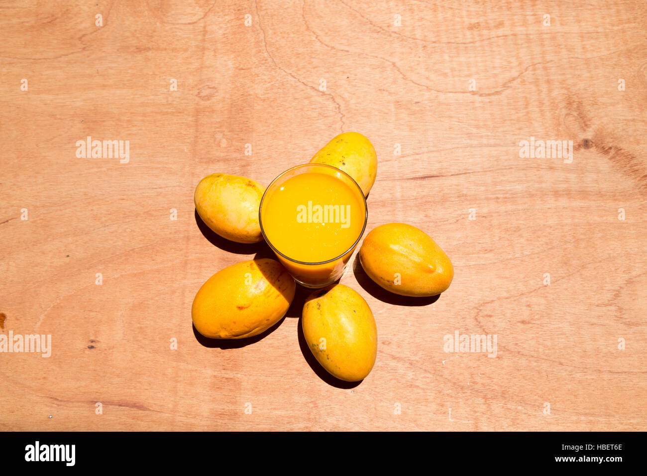 Jaune à maturité paraguayenne de mangues et de tasse de jus de mangue fraîche sur la table en bois, sous le soleil de couleurs vives, de mise à plat Banque D'Images