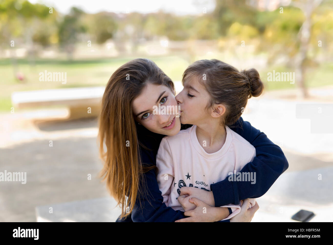 Fille de donner un baiser à sa sœur aînée, assis dans un parc. Banque D'Images