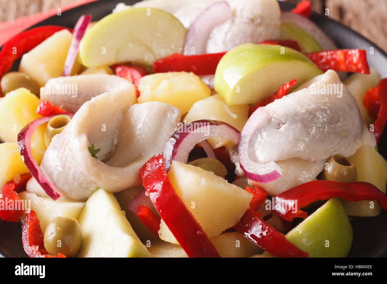 Maison de vacances salade de Harengs aux pommes de terre, pomme, l'oignon, le poivre et les olives macro sur une plaque horizontale. Banque D'Images