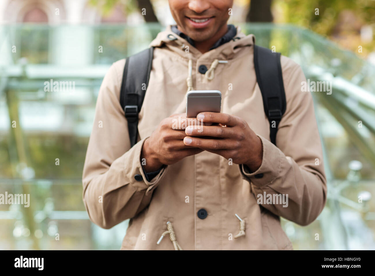 Portrait de jeune homme teint foncé avec sac à dos en utilisant son portable dans la rue. Banque D'Images