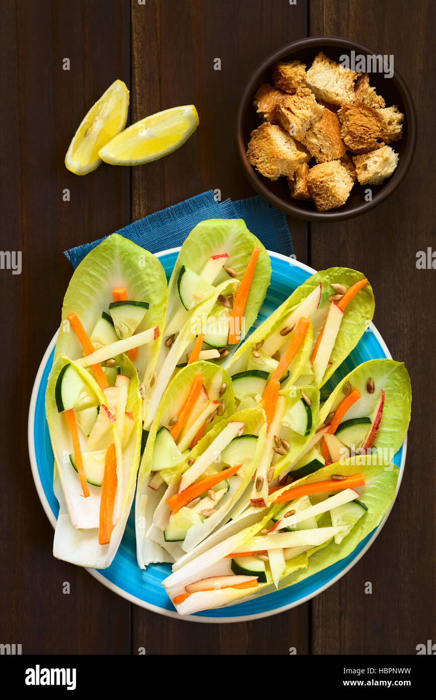 Salade fraîche de feuilles d'endive, concombre, carotte, pomme et graines de tournesol, de croûtons et de quartiers de citron au-dessus Banque D'Images