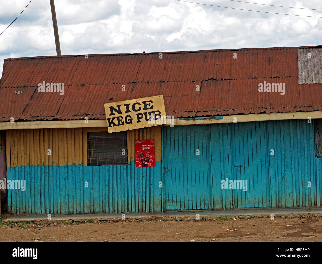 Tôle ondulée roadside shack peint en jaune et bleu foncé avec une fenêtre et panneau 'nice fût pub' au Kenya Afrique Banque D'Images