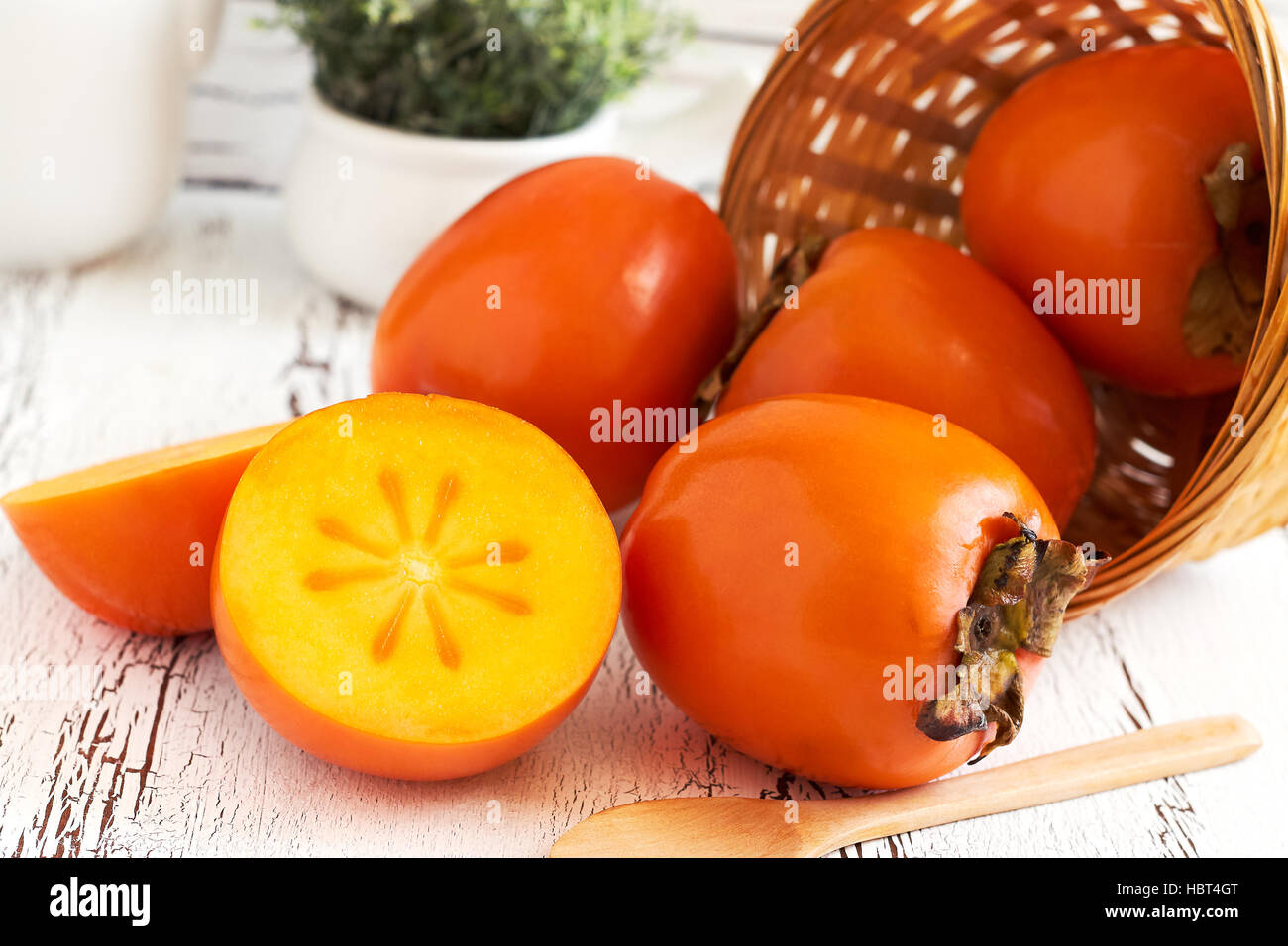 (Japanese persimmon Diospyros kaki) dans panier tressé blanc sur fond de bois rustique Banque D'Images