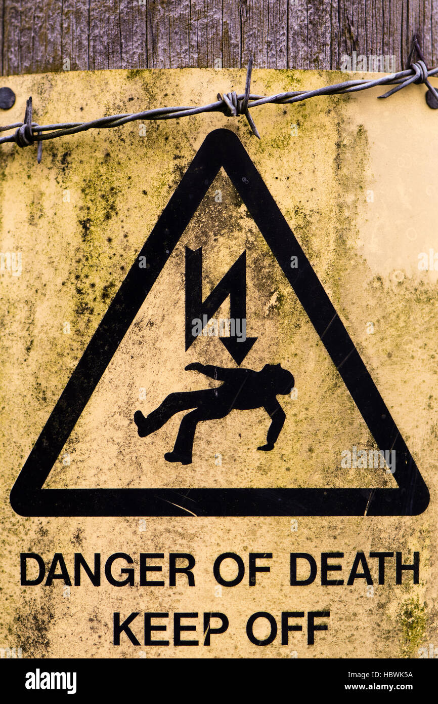 Danger de mort signe et barbelés. Panneau d'avertissement jaune sur poteau d' électricité, couverts d'algues et la crasse Banque D'Images