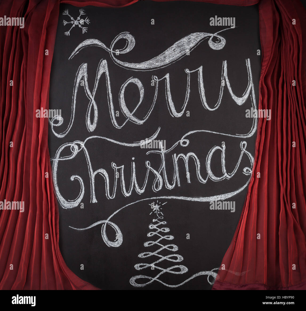 Joyeux Noël lettrage dessiné à la main avec de la craie sur tableau noir encadré par des rideaux rouges. Élégant design unique avec des flocons de neige et l'arbre de Noël Banque D'Images