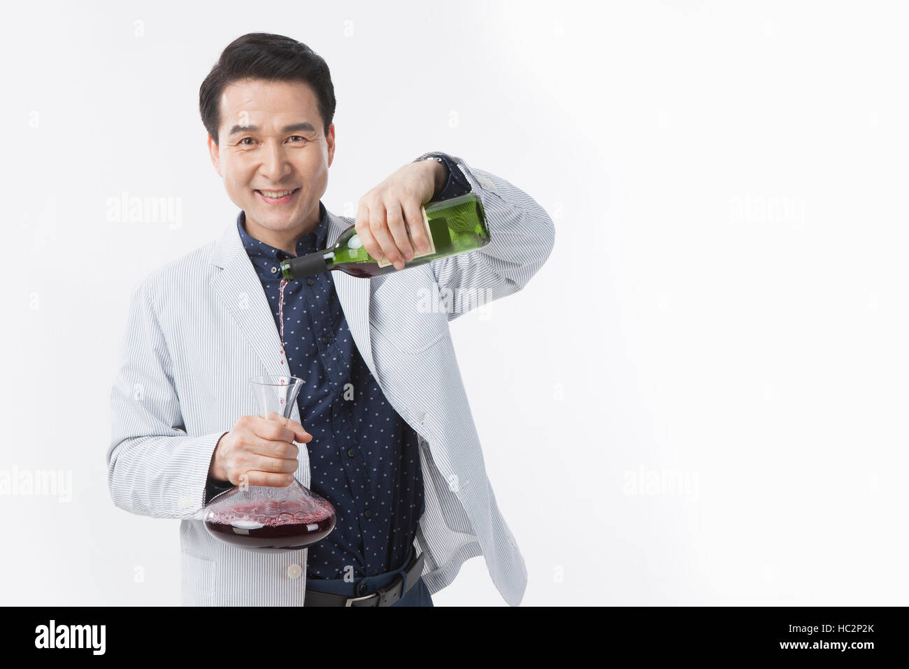 Smiling middle aged man pouring red wine à partir de la bouteille dans la carafe Banque D'Images