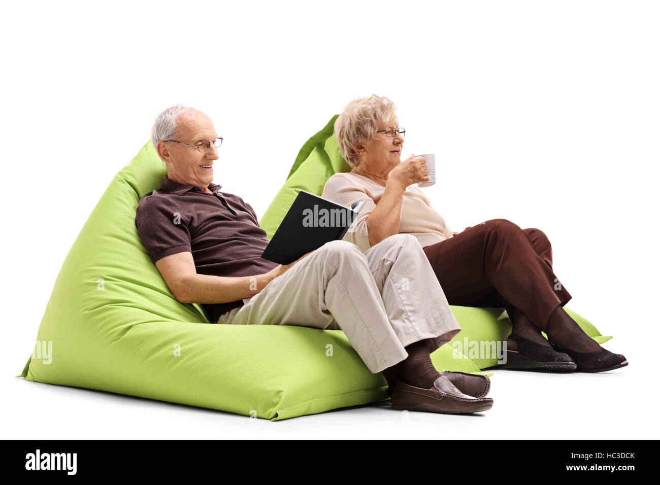 Un homme âgé assis sur un pouf poire et la lecture d'un livre avec une  femme âgée assise sur un pouf poire et boire d'une tasse isolé sur fond  blanc Photo Stock -