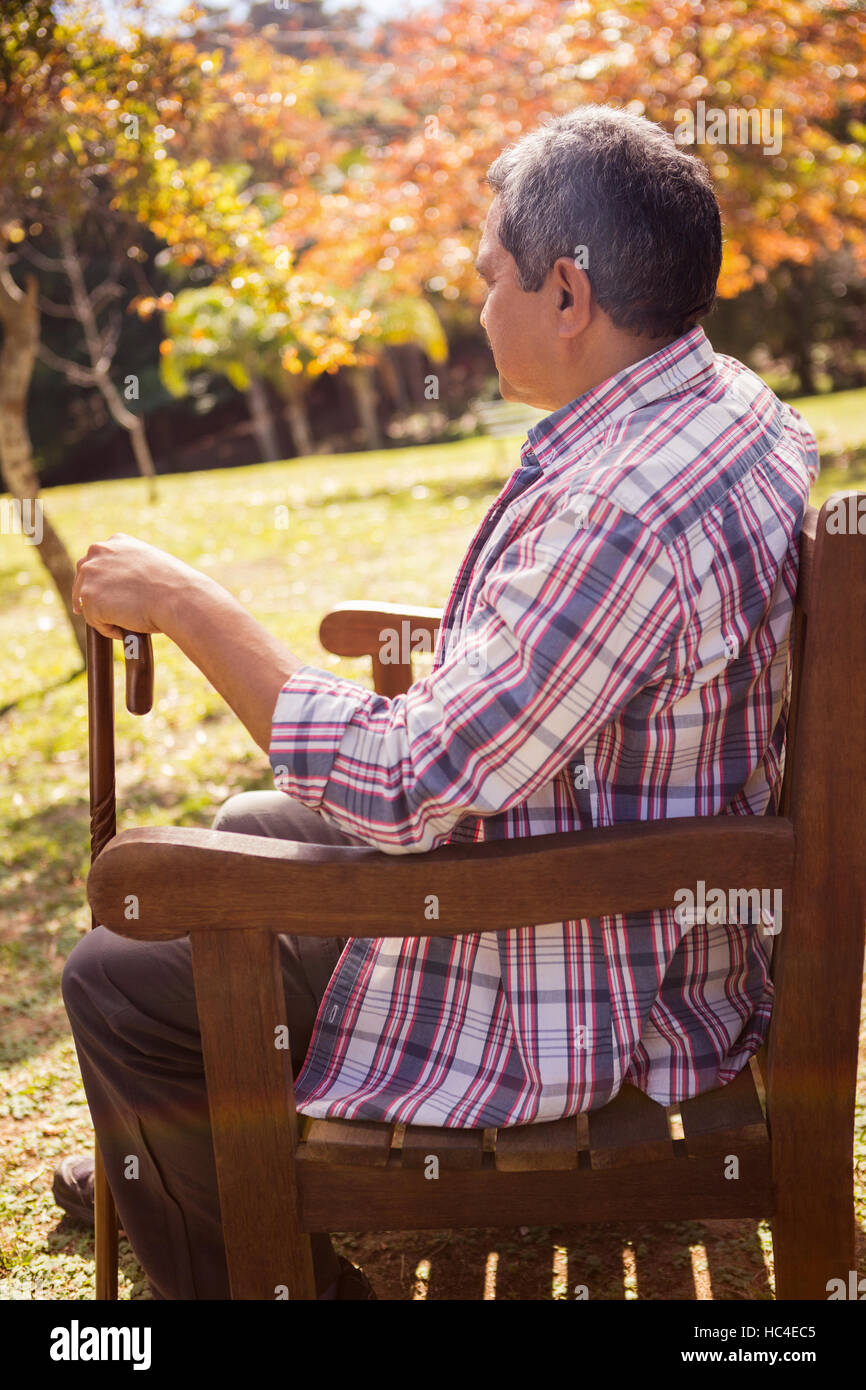 Un homme âgé assis sur un banc avec sa canne Banque D'Images