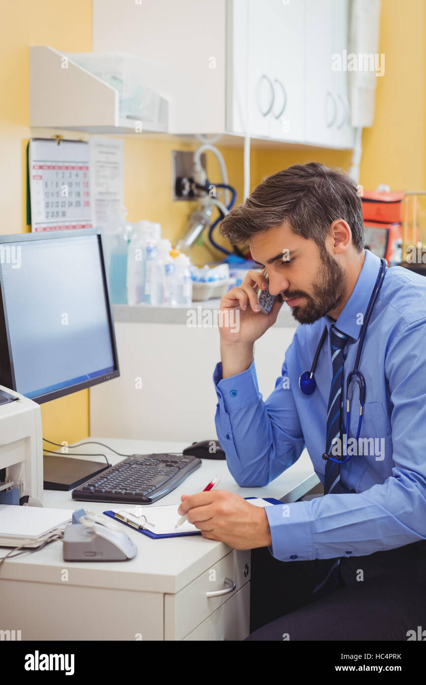 Médecin assis à son bureau et parlant au téléphone Banque D'Images