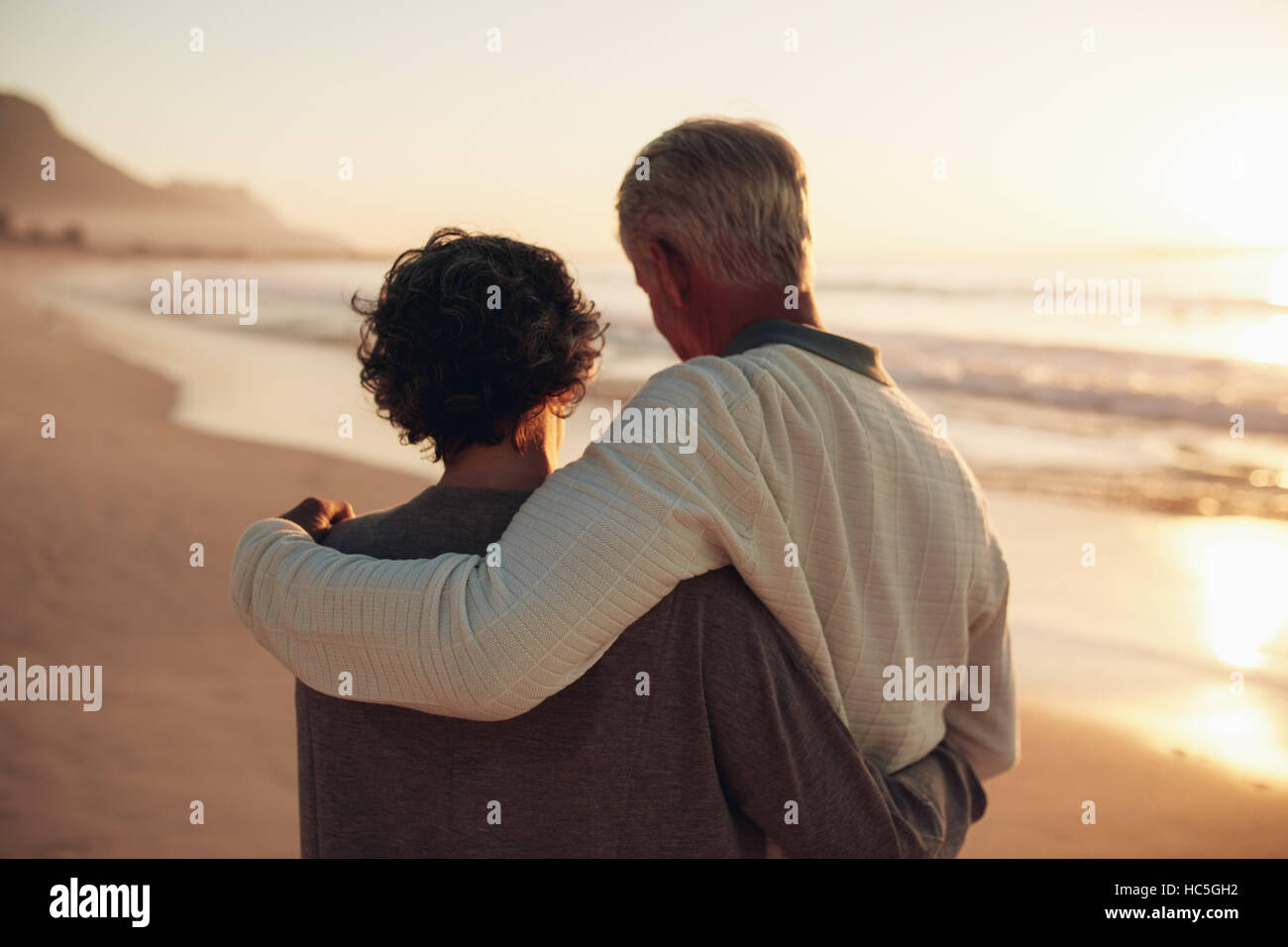 Vue arrière Vue d'un couple au bord de la mer. Smiling mature couple tranquille de dépenser du temps sur la plage au coucher du soleil. Banque D'Images