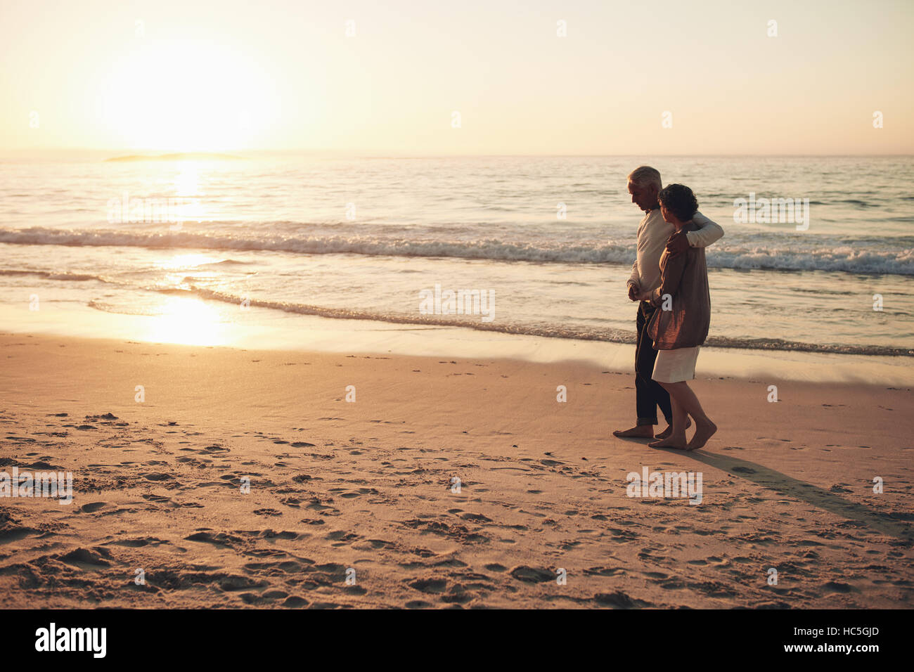 Photo de couple sur la plage au coucher du soleil. Senior et senior femme en promenade au bord de la mer. Banque D'Images