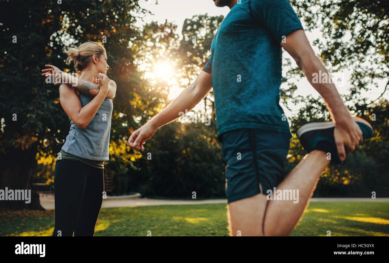 Shot of young man and woman doing stretching exercice dans le parc. Jeune couple en préchauffage pour exercices du matin. Banque D'Images