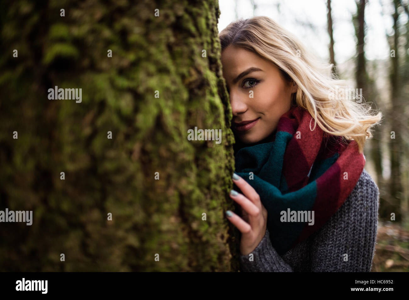 Belle femme se cachant derrière tronc de l'arbre dans la forêt Banque D'Images