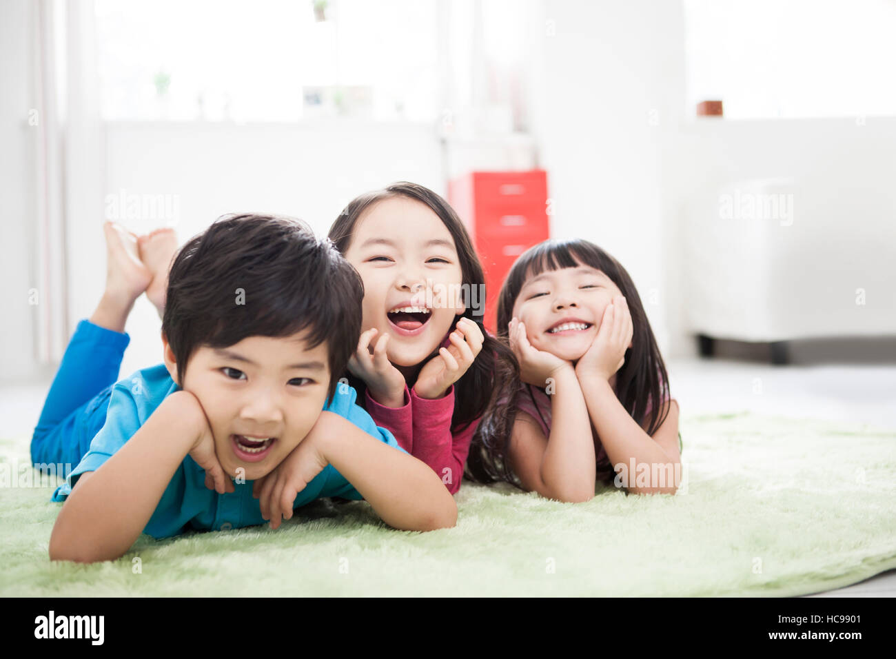 Trois enfants souriants qui est orientée vers le bas en plaçant les mains sur le menton sur un tapis Banque D'Images