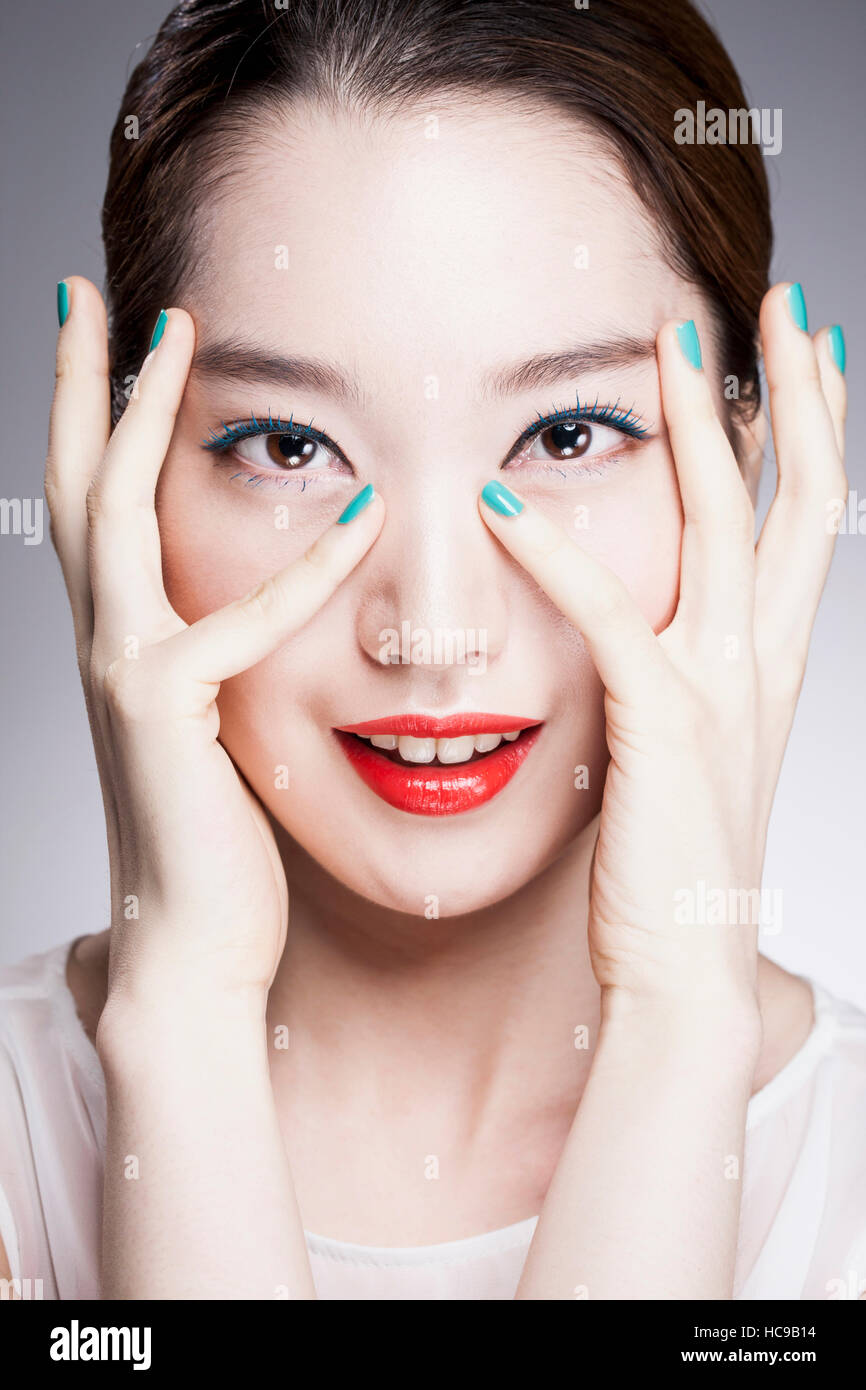 Portrait of young smiling woman with red lips coréen et les ongles bleu enveloppant son visage avec ses mains Banque D'Images