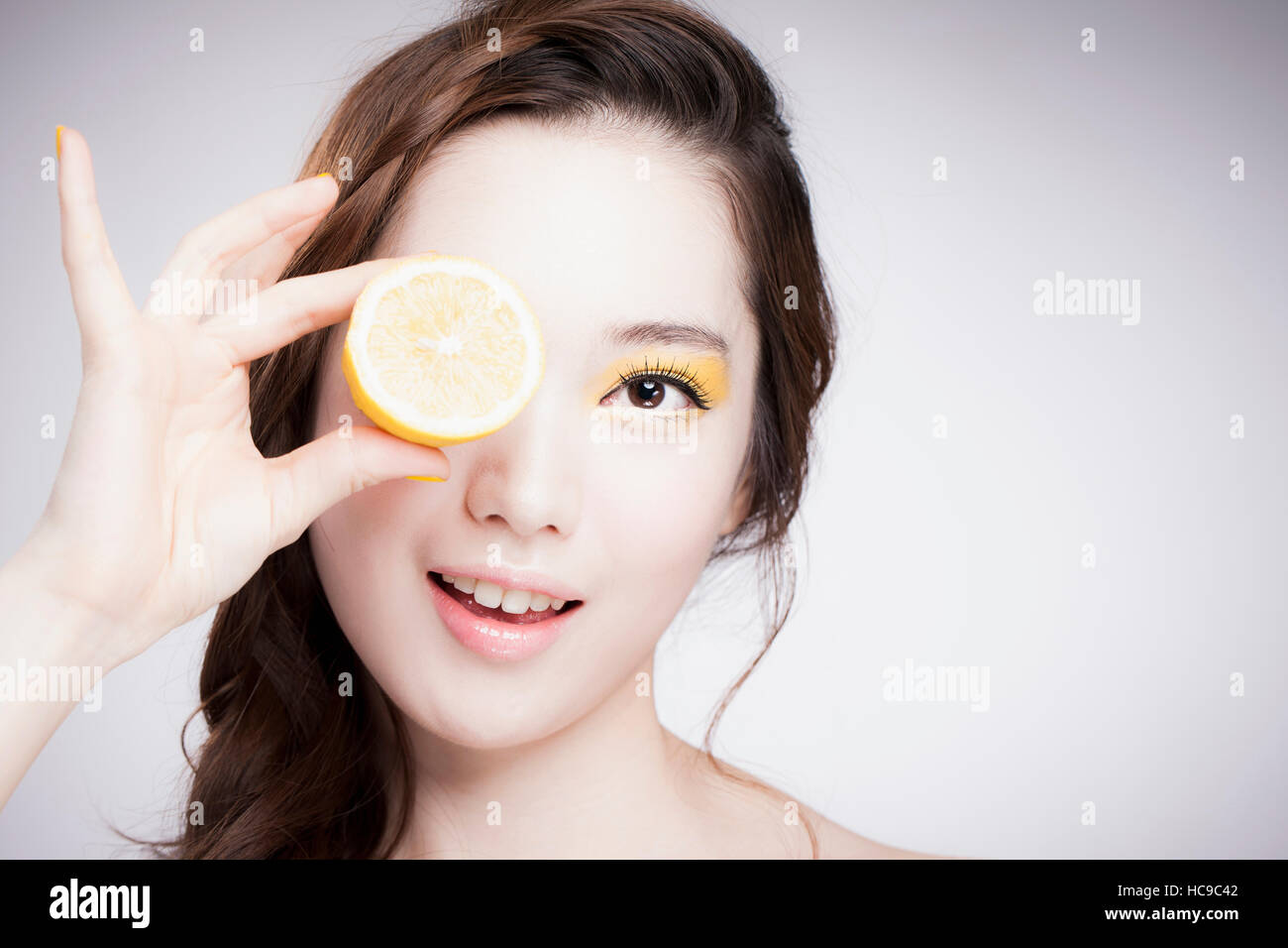 Portrait of young smiling woman coréen dans l'ombre d'oeil jaune couvrant son œil présentant une section de citron Banque D'Images