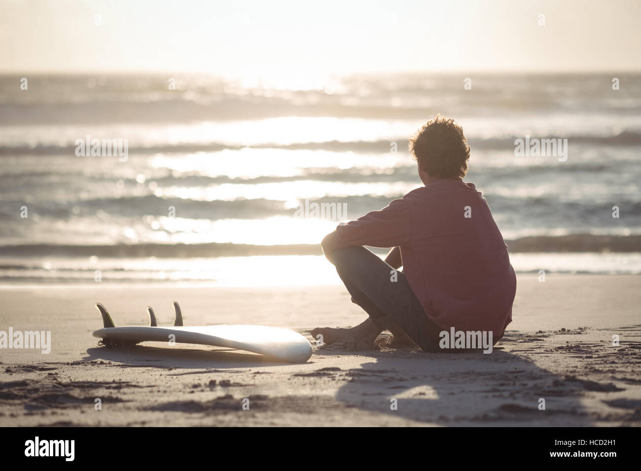 Man with surfboard sitting on beach Banque D'Images