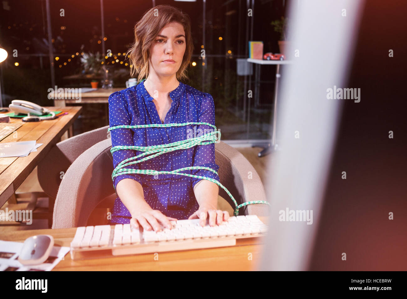 Businesswoman tied avec corde tout en travaillant au bureau Banque D'Images