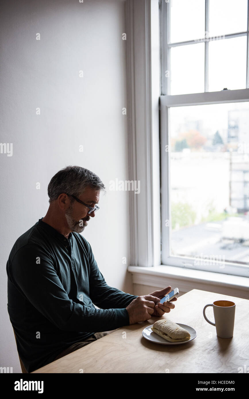 L'homme assis à table et à l'aide de mobile phone Banque D'Images