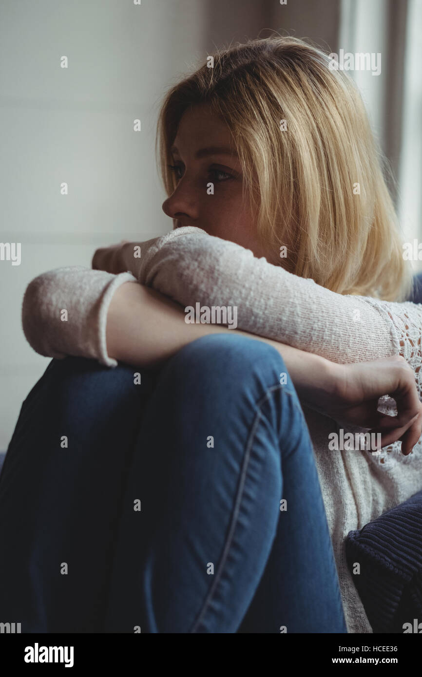Thoughtful woman sitting on sofa in living room Banque D'Images