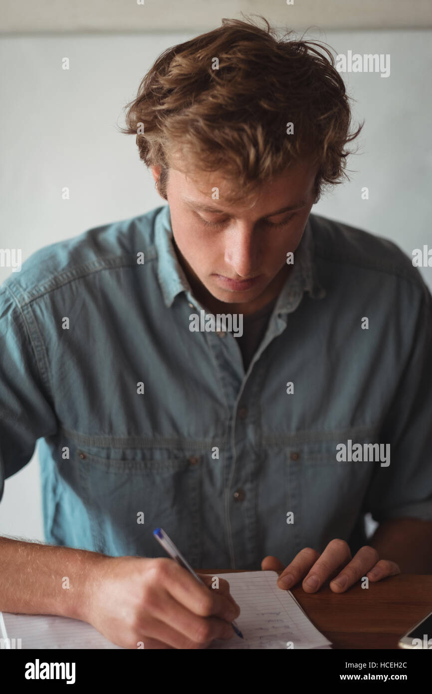 Man sitting at desk writing on notebook Banque D'Images