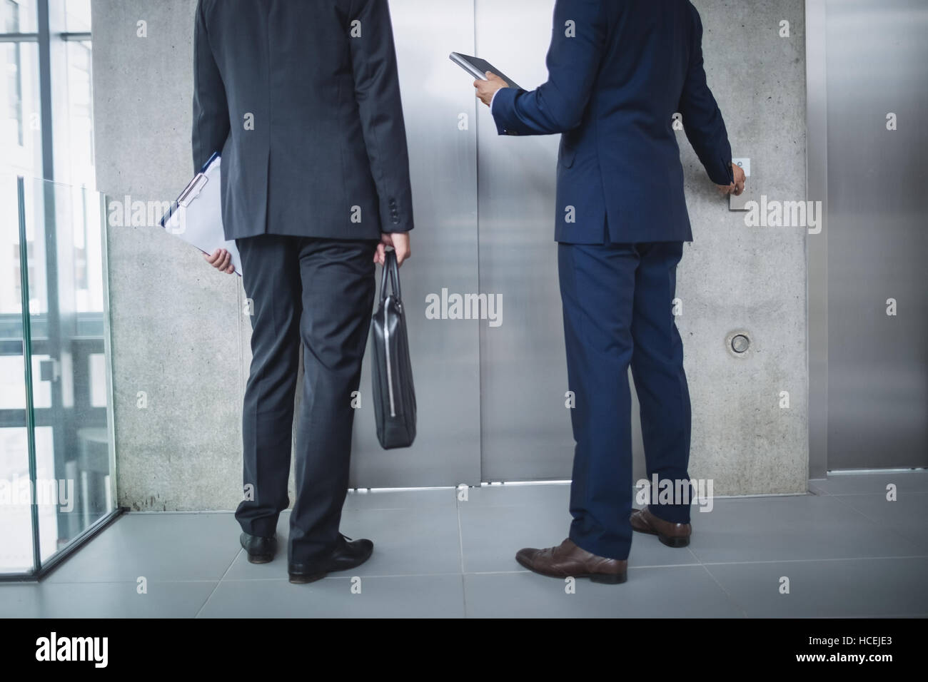 Businessmen standing par l'ascenseur et appuyer sur le bouton Banque D'Images