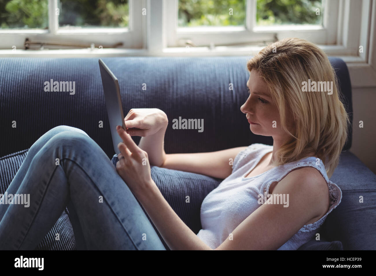 Belle femme assise sur un canapé et using digital tablet in living room Banque D'Images