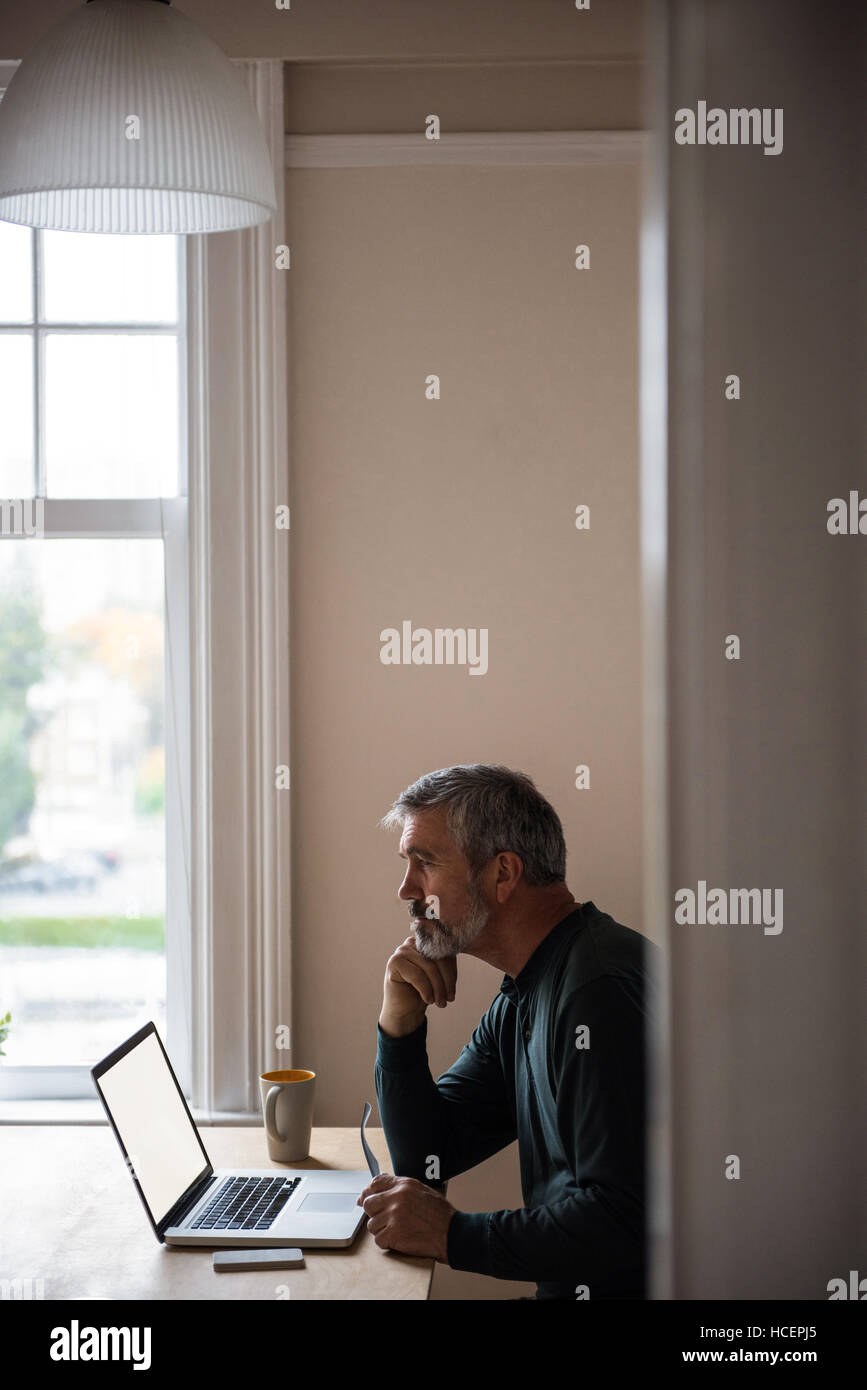 Thoughtful man sitting with laptop in living room Banque D'Images