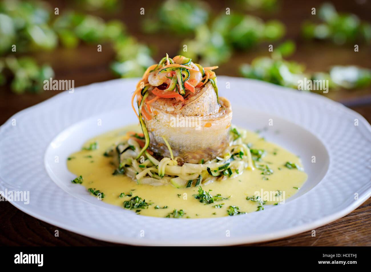 Rouleau de poissons et crevettes avec sauce crémeuse aux herbes, légumes sur une plaque blanche Banque D'Images