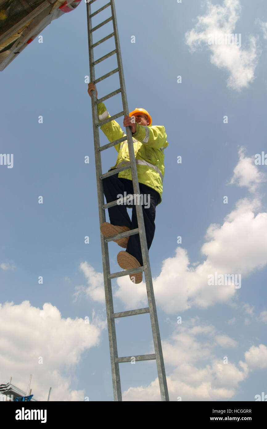 Un travailleur de la construction grimpe une longue échelle en acier. Photographié par en dessous avec bleu ciel nuageux, avec en arrière-plan. Banque D'Images