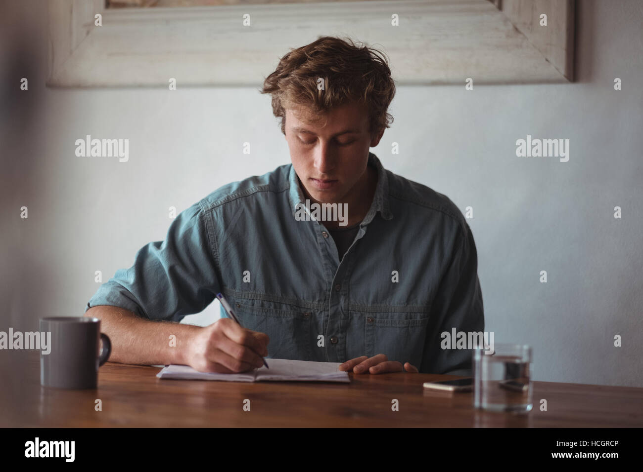 Man sitting at desk writing on notebook Banque D'Images