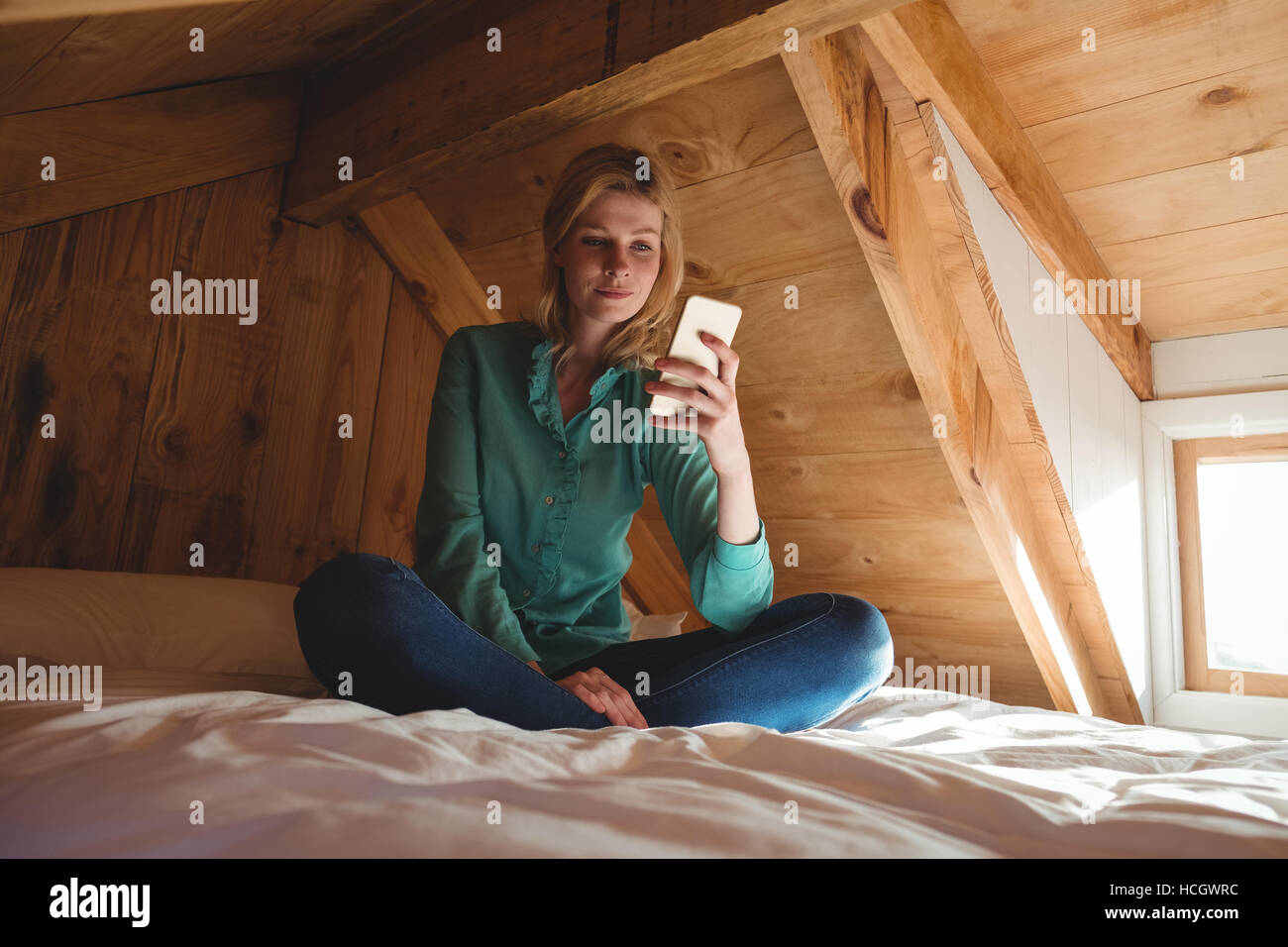 Beautiful woman sitting on bed and using mobile phone in bedroom Banque D'Images