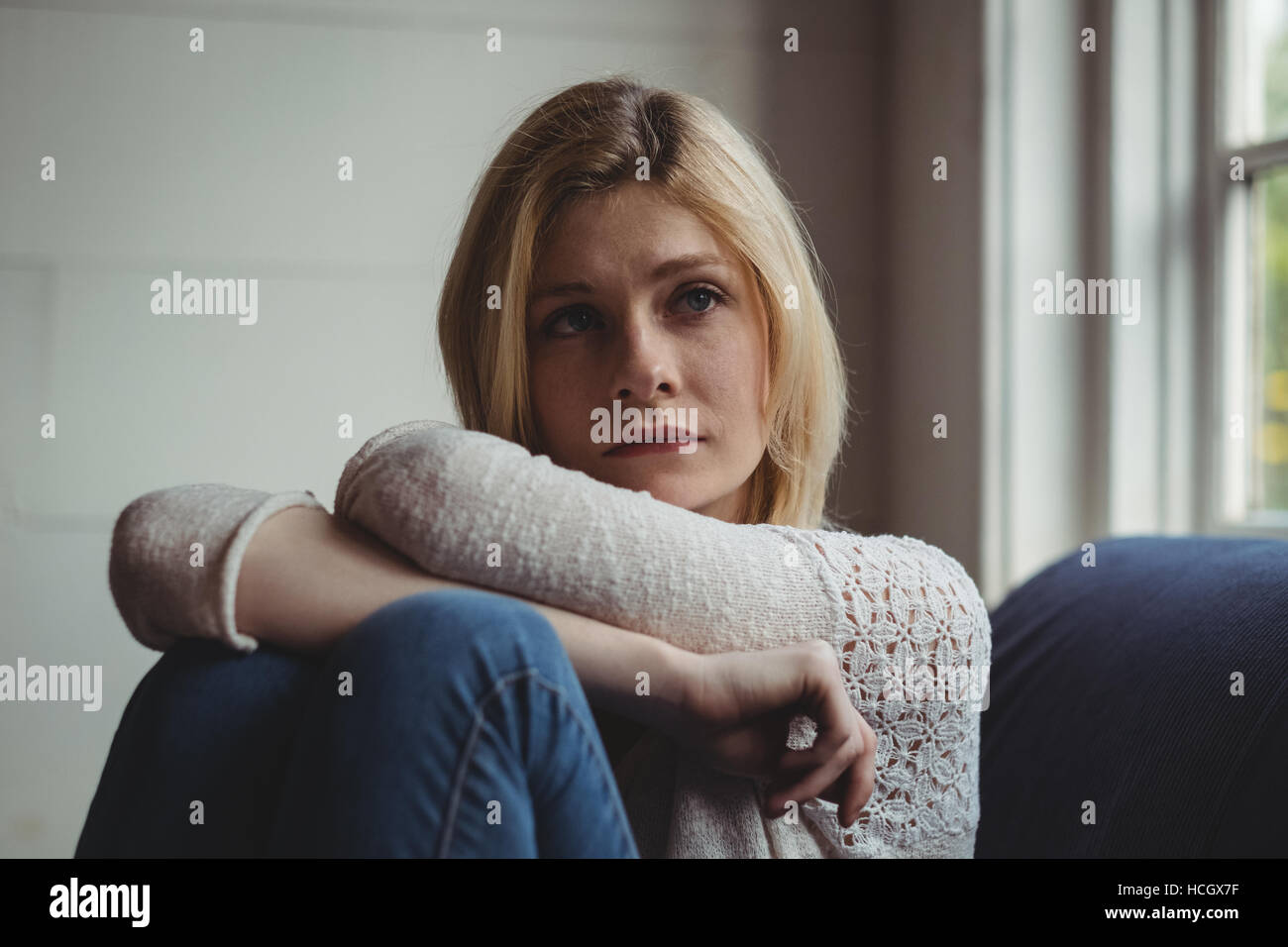Thoughtful woman sitting on sofa in living room Banque D'Images