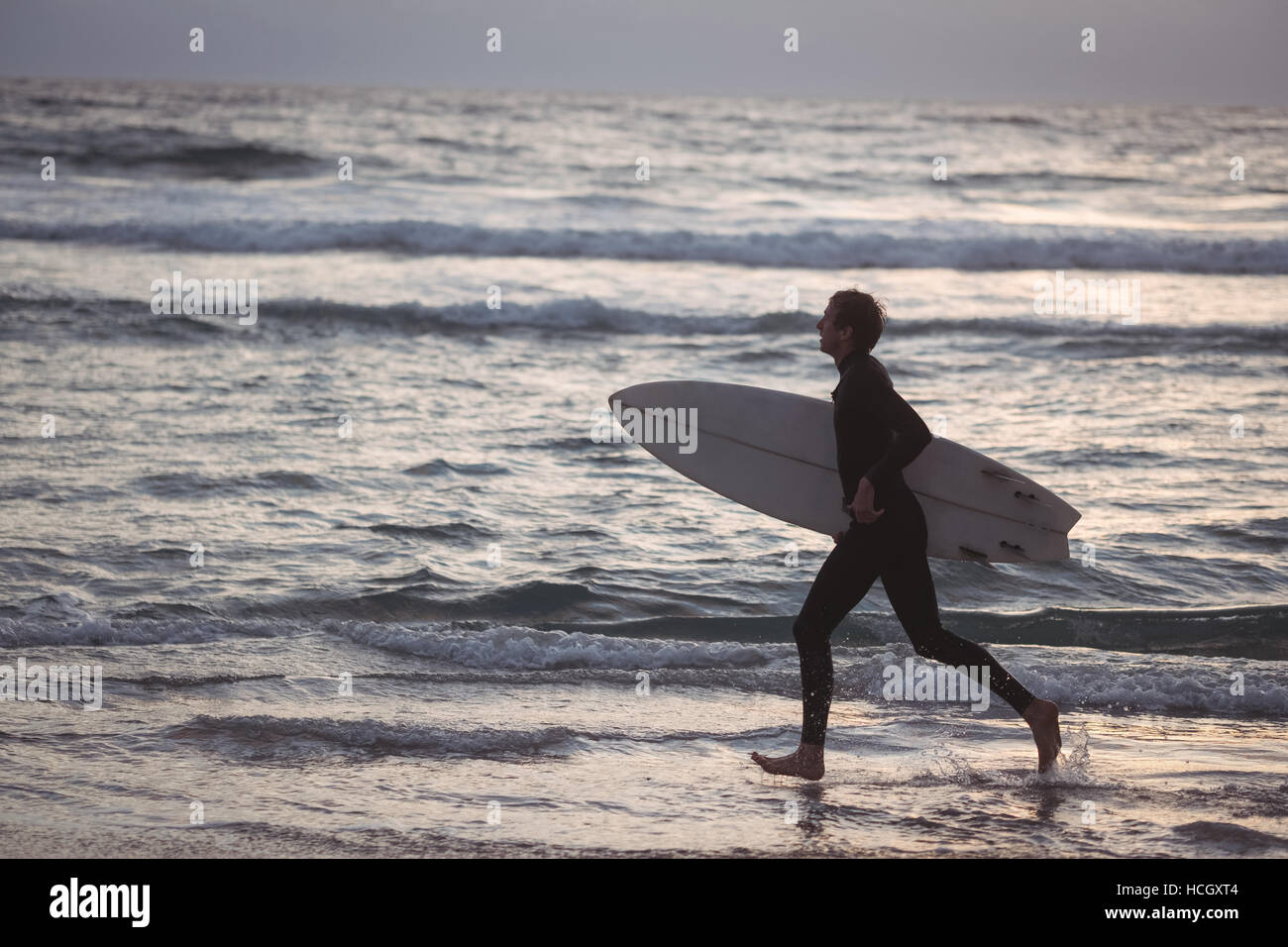 Man carrying surfboard running on beach Banque D'Images