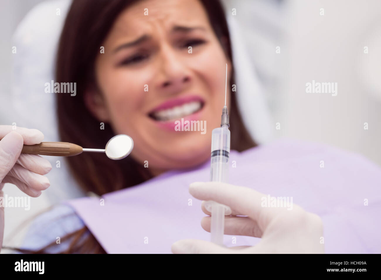 Dentiste tenant une seringue dans l'avant du patient effrayé Banque D'Images