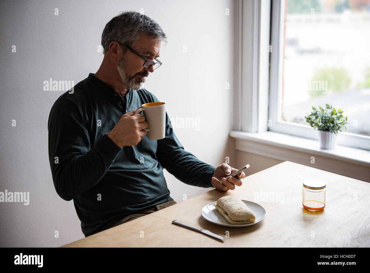L'homme à l'aide de téléphone mobile tout en ayant une tasse de café Banque D'Images