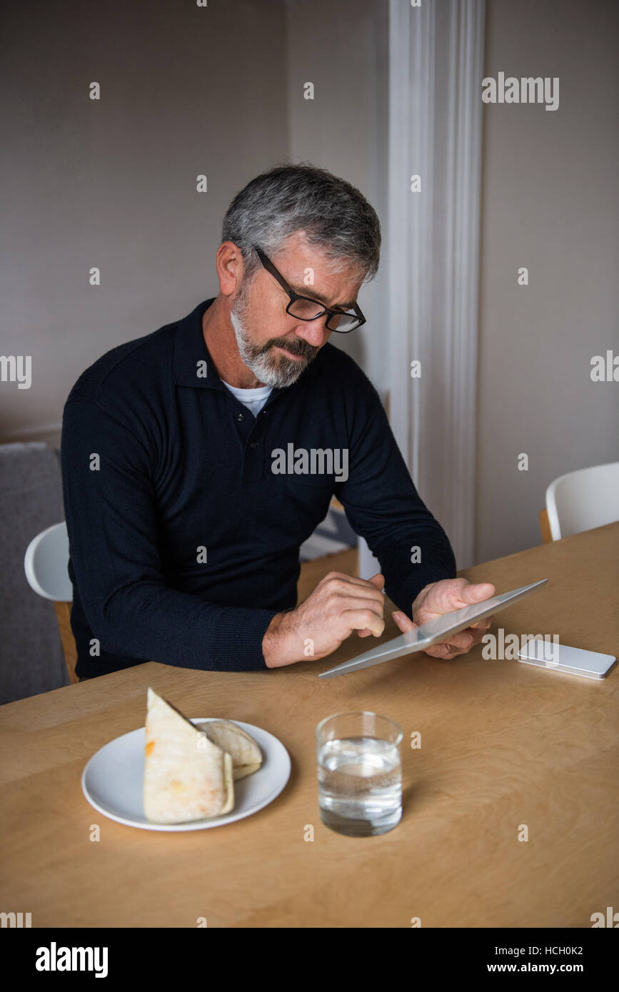 L'homme assis à table et using digital tablet Banque D'Images