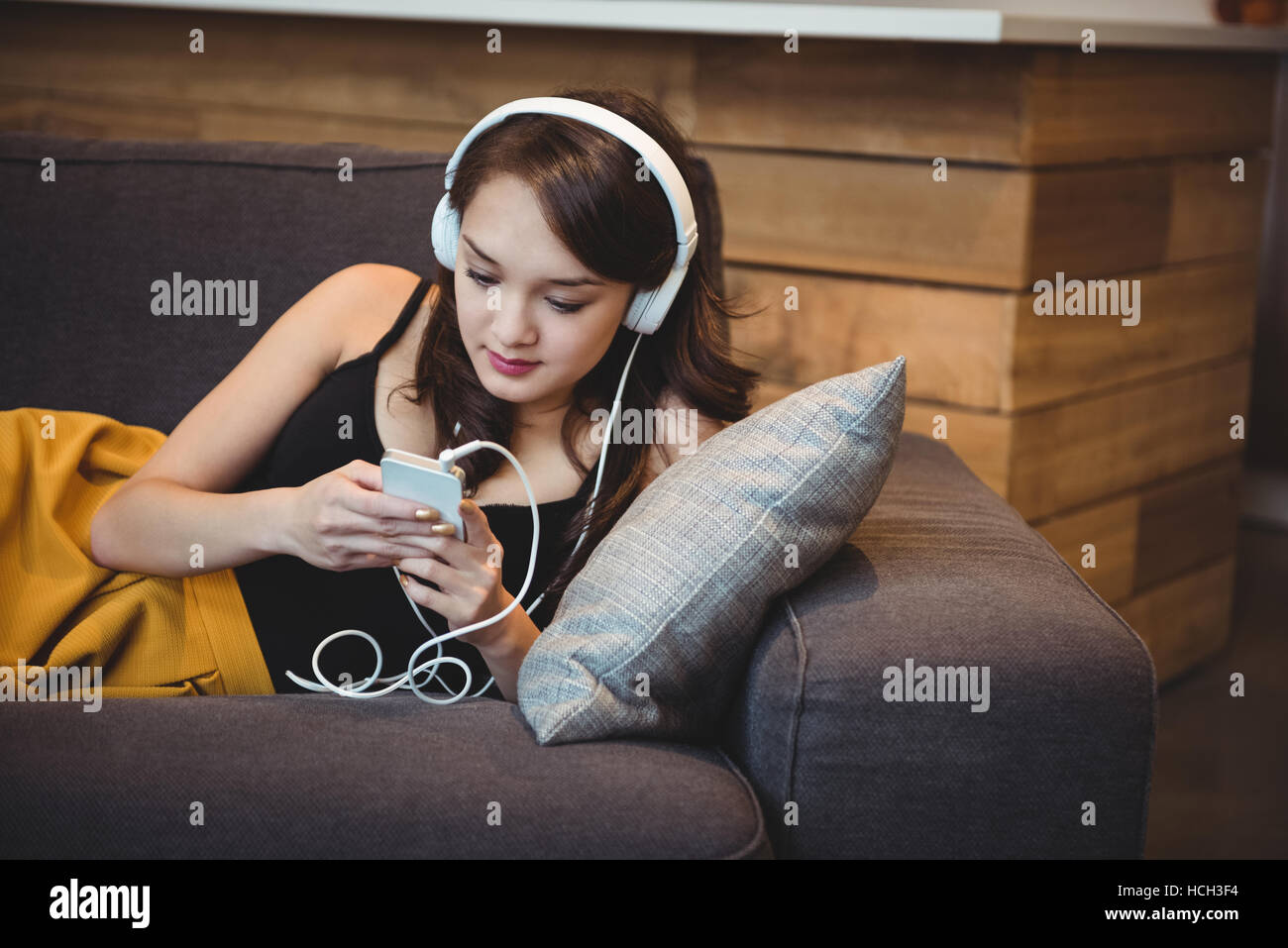 Femme couchée sur le canapé tout en écoutant de la musique avec un téléphone mobile Banque D'Images